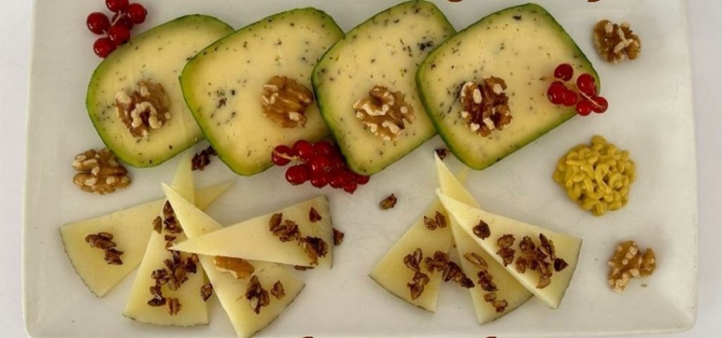 Craxi Spiced Gouda Cheese. Artisan Gouda with a flavorful blend of green pesto spices, and Manchego cheese served on a cheese board.