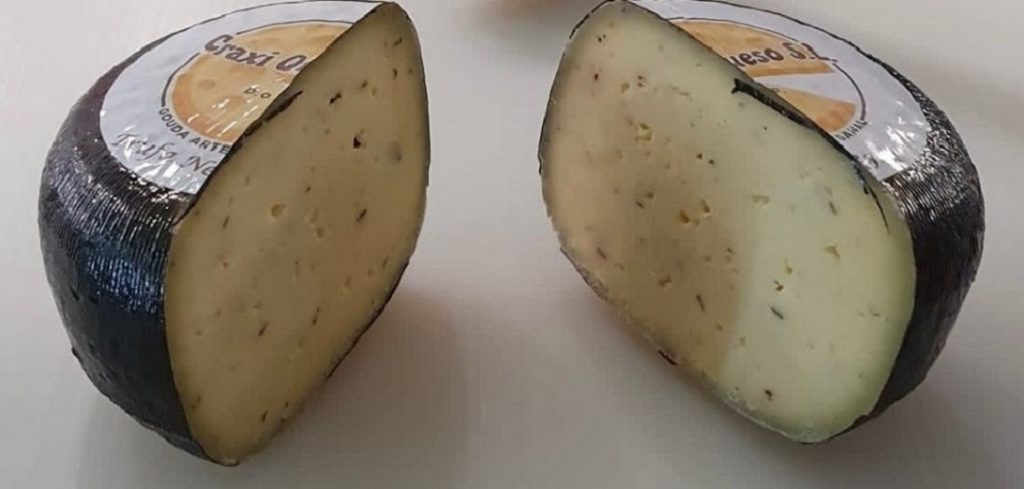 Close-up of a halved Craxi Gouda truffle cheese, made from raw cow's milk and blended with aromatic black truffle shavings.